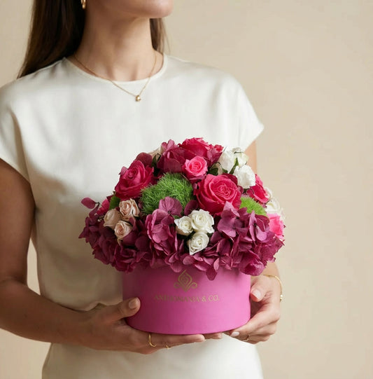 model holding hydrangeas and roses in a hot pink small hat box with pink and white blooms