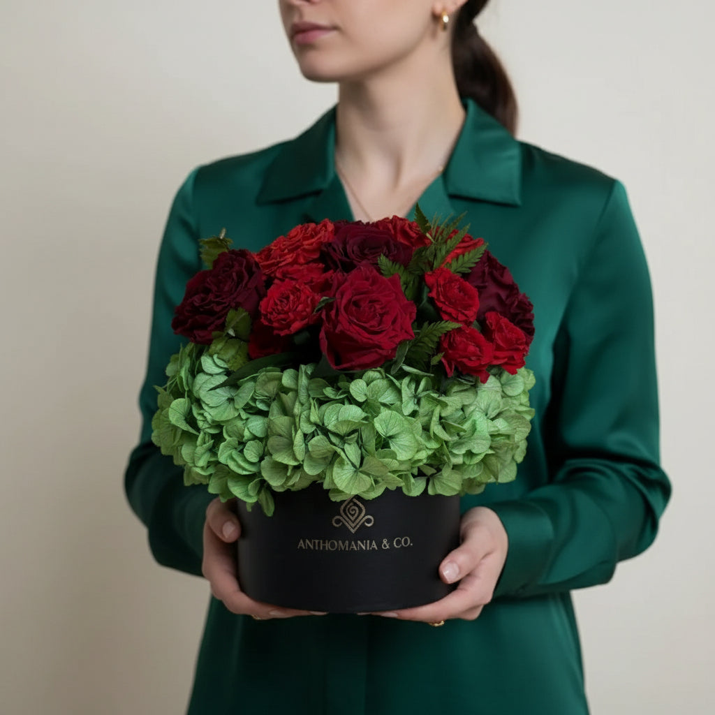 model holding hydrangeas and roses in a black small hat box with red and light green blooms