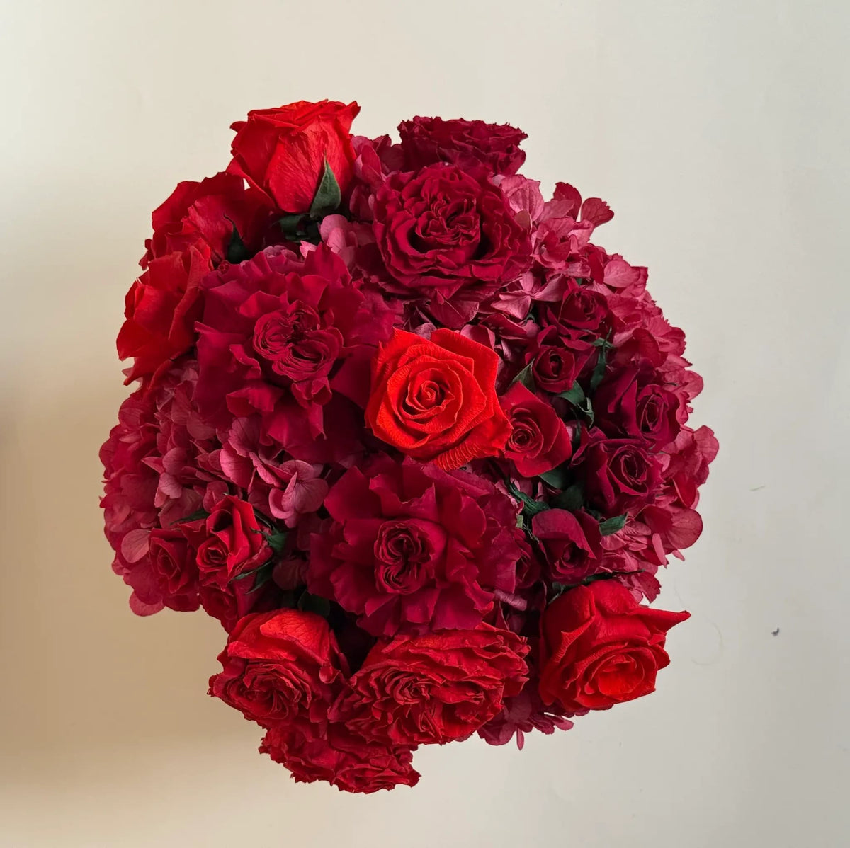 top view of hydrangeas and roses forming a red dome inside a large black hat box