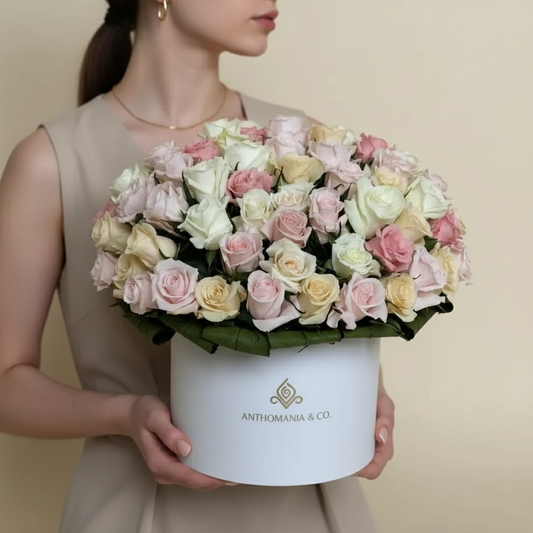 Person holding a bouquet of pastel-colored roses in a white box with 'Anthonymania & Co.' branding.