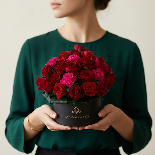 model holding mini roses in a black small hat box with pink and red blooms