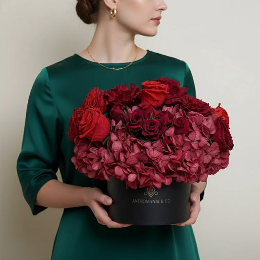 model holding hydrangeas and roses in a large black hat box filled with red blooms
